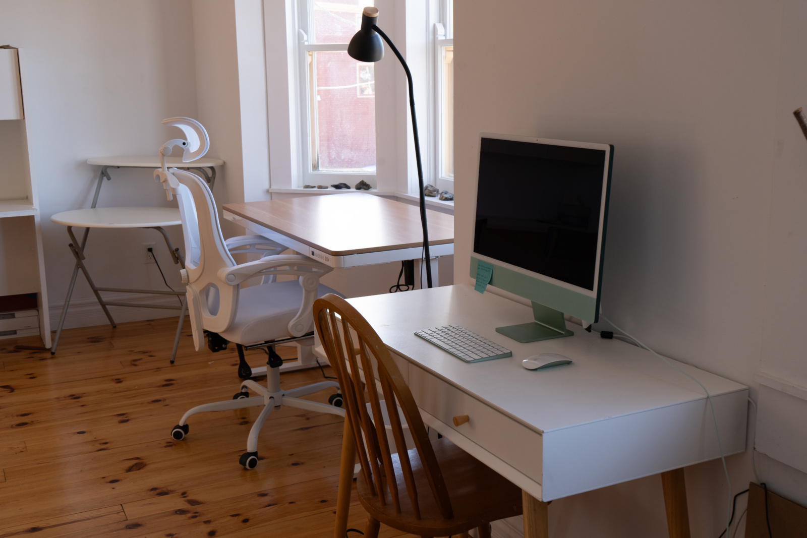 A corner desk, the standing desk in front of a bay window, and the computer desk with a Mac set up.