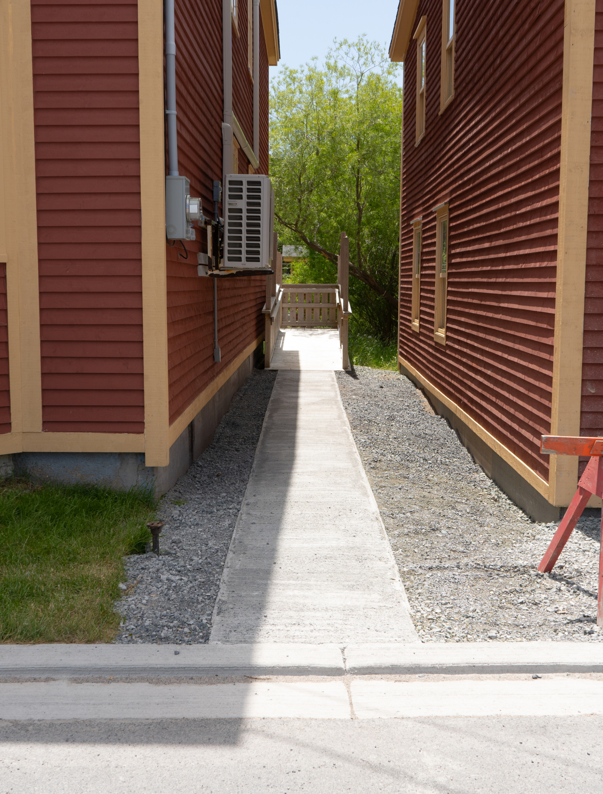Concrete path leading to the back of our red building via wheelchair ramp, shown in sunlight.