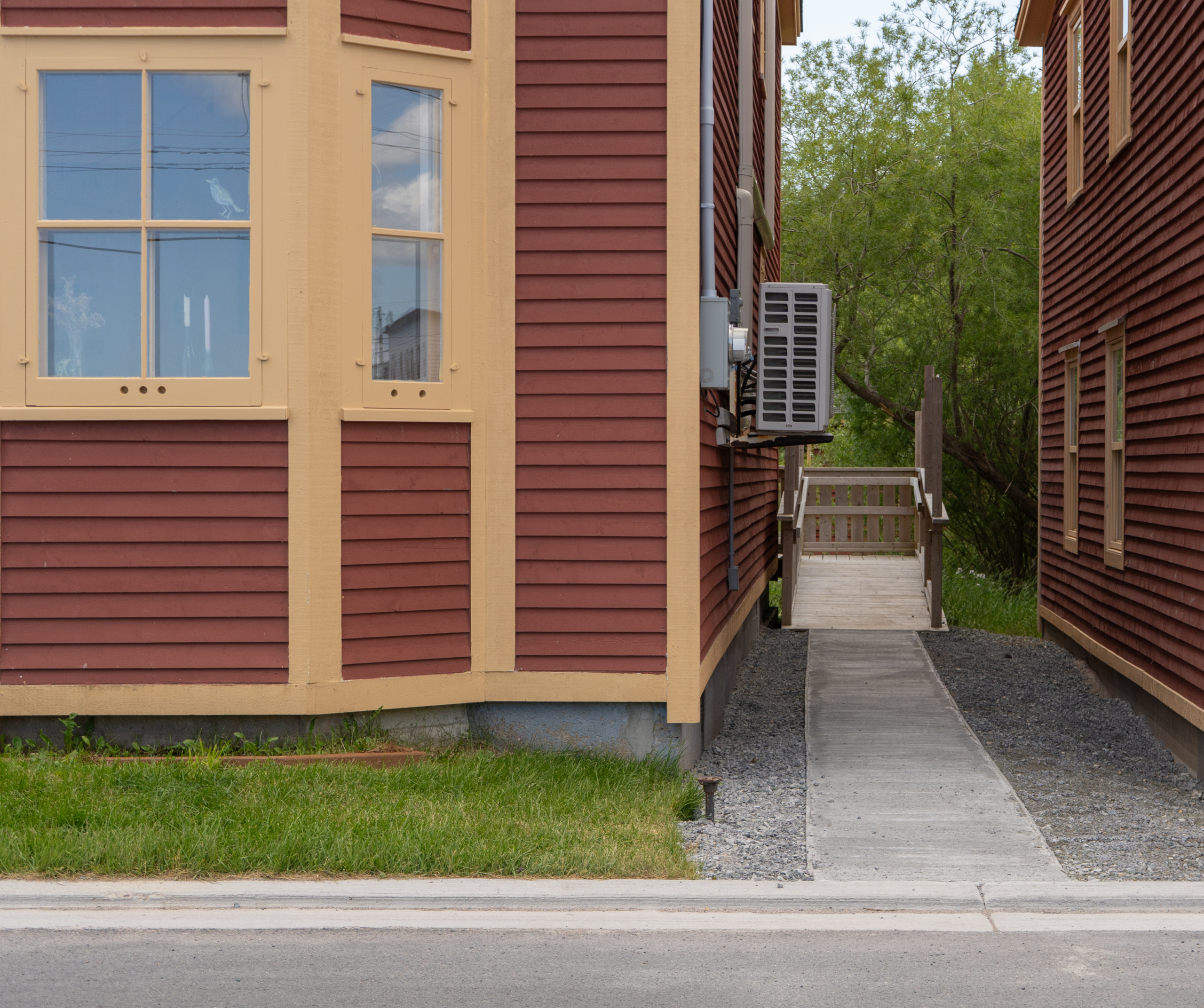 Red building seen from the front. The right side is shown, with a concrete path leading to a wooden wheelchair ramp connected to the back of the building.