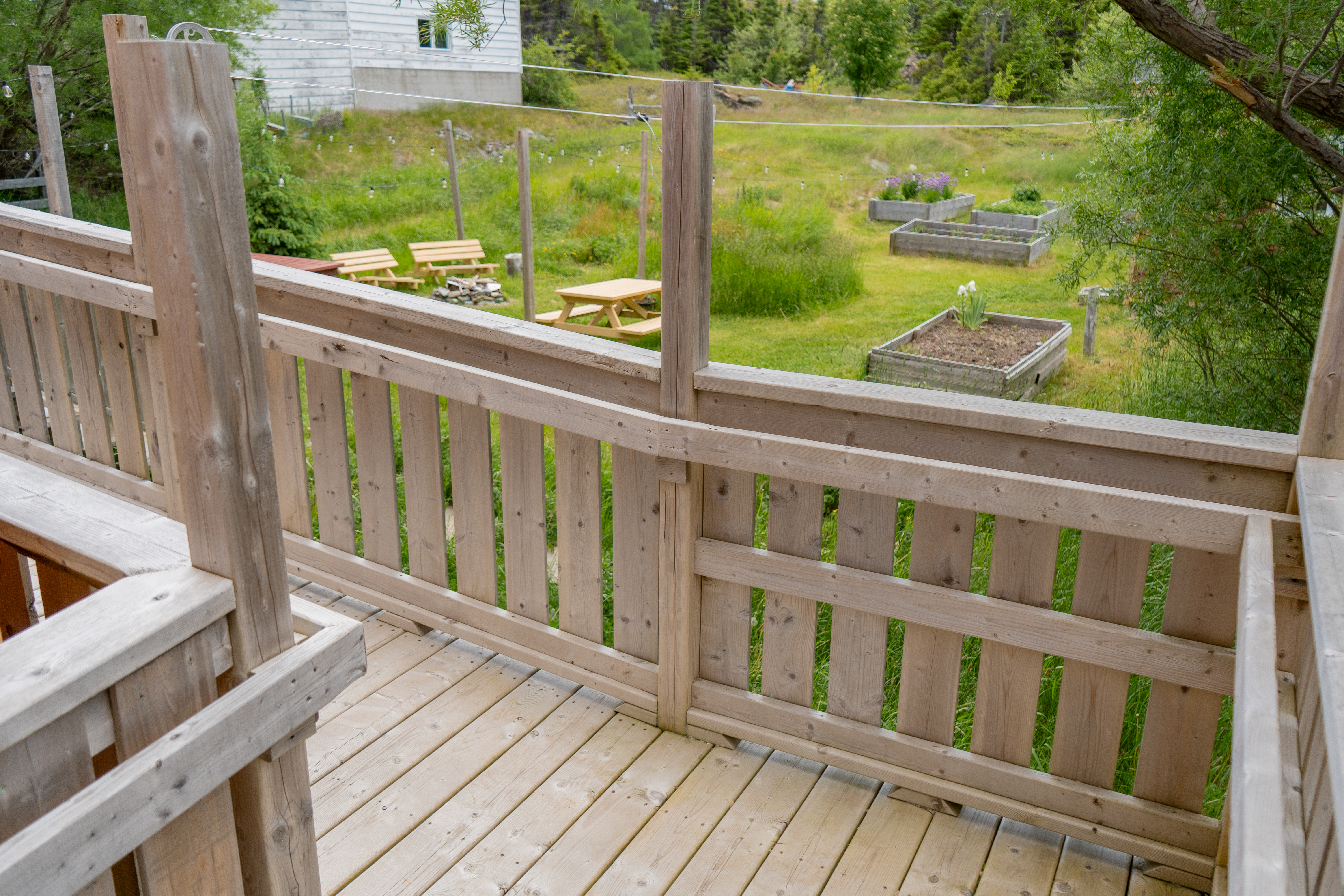 The garden, with benches and wooden garden beds, viewed from over the wheelchair ramp's handrail, from the corner leading to the patio