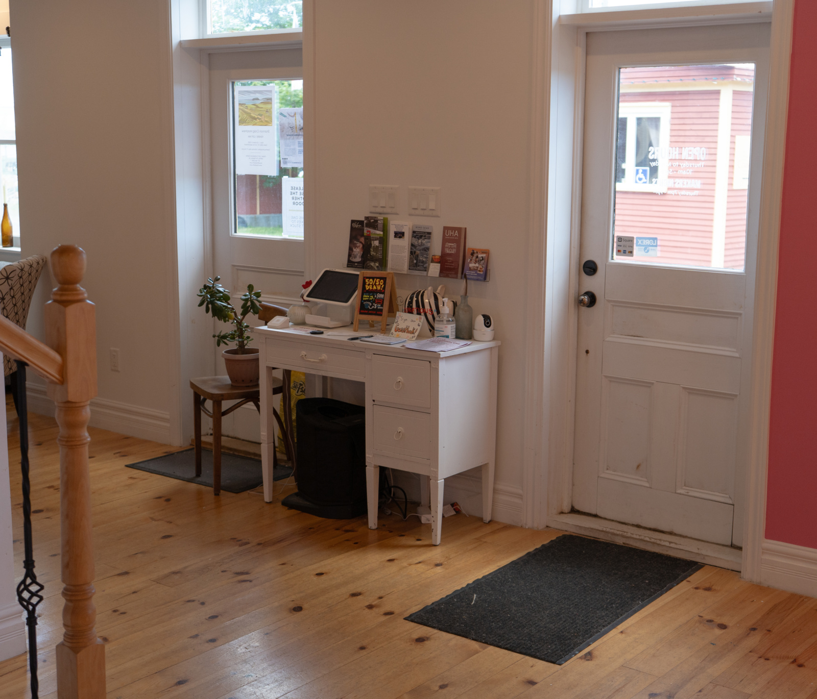 Two doors with door mats at the front entrance of the building, with a desk holding pamphlets and donations between the two.